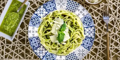 Deliciosa pasta con pesto, ideal para tus recetas de pasta con pesto. Servida en un plato decorado con un toque mediterráneo.