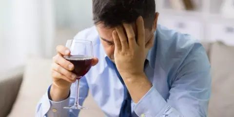 Hombre con copa de vino tinto, con la mano en la frente, buscando alivio en un vino sin histamina.