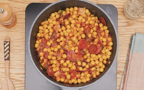 Garbanzos fritos con chorizo y bacon en sartén, listos para servir. Un plato sabroso y reconfortante.