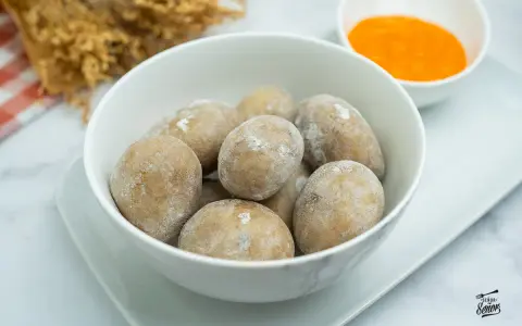 Un tazón blanco lleno de papas arrugadas, cubiertas de sal, junto a un pequeño cuenco con mojo rojo.