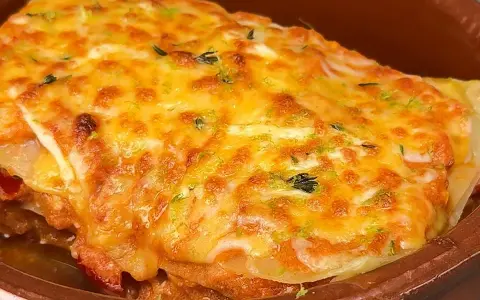 Deliciosa lasaña de atún gratinada con queso dorado y hierbas frescas, servida en un cuenco de barro.
